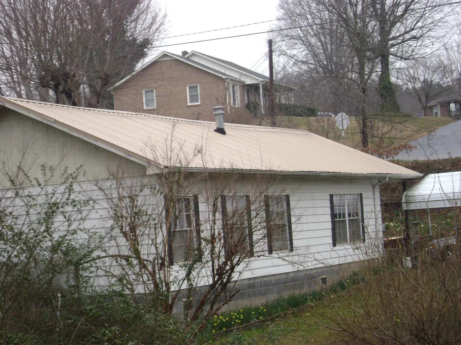 Tan metal roof on a white sided house set into a hillside — Commercial Roofing by Roofing Brothers in Wilmington